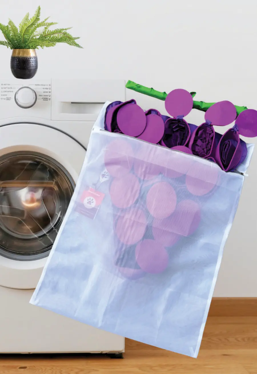 A PawzNDogz laundry mesh bag carrying a Forbidden Grapes™ Snuffle Mat, also from PawzNDogz. A washing machine sits in the background out of focus.
