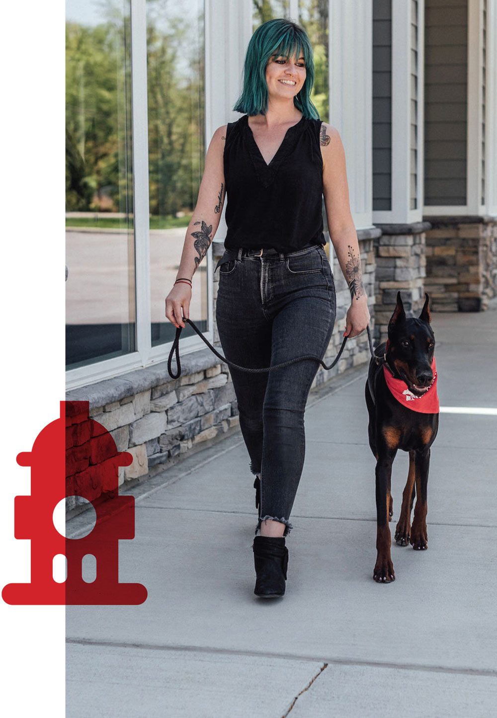 A woman with blue-green hair and tattoos walks a Doberman Pinscher on a leash.