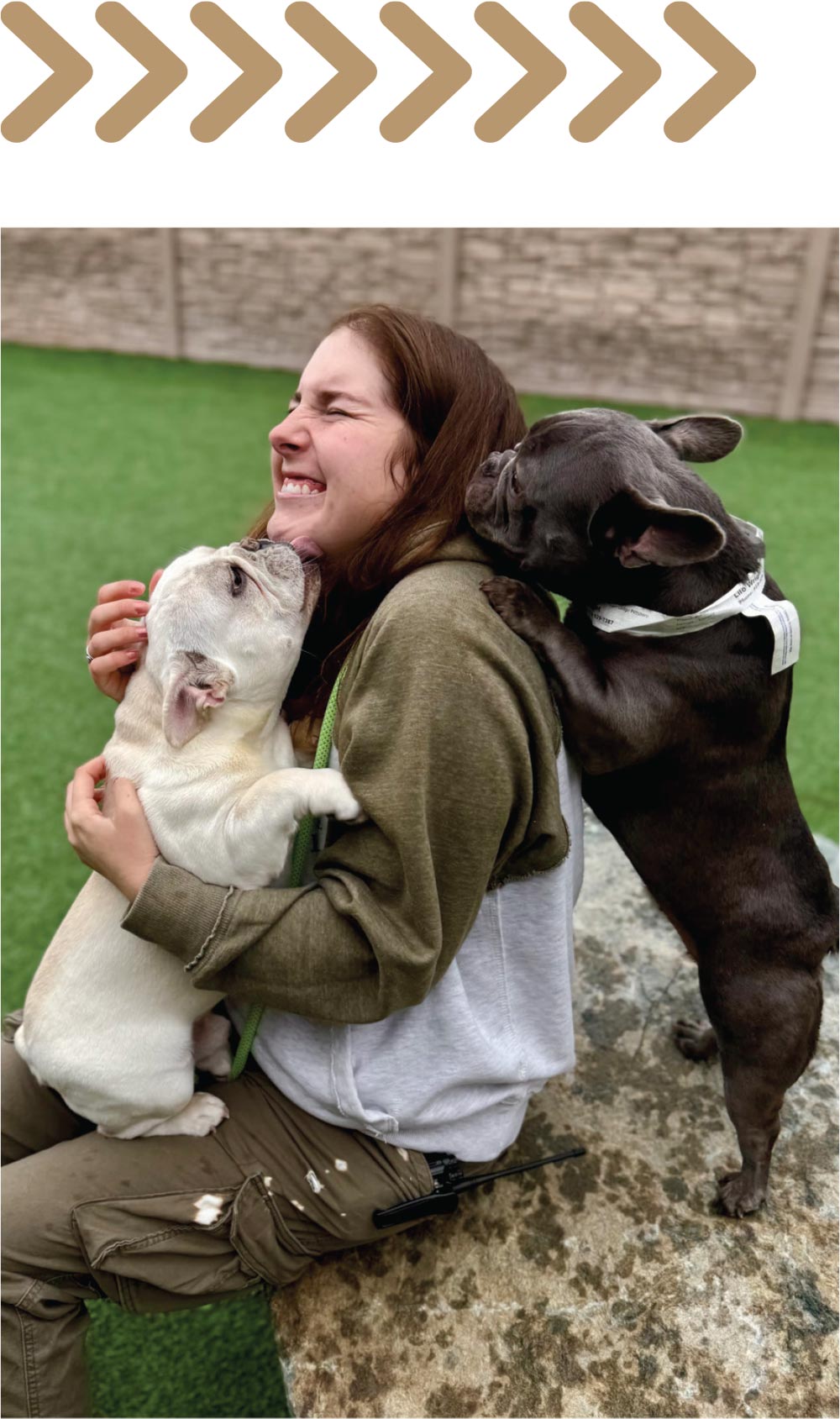 Woman sitting outdoors being affectionately kissed by two French Bulldogs, one black and one white.