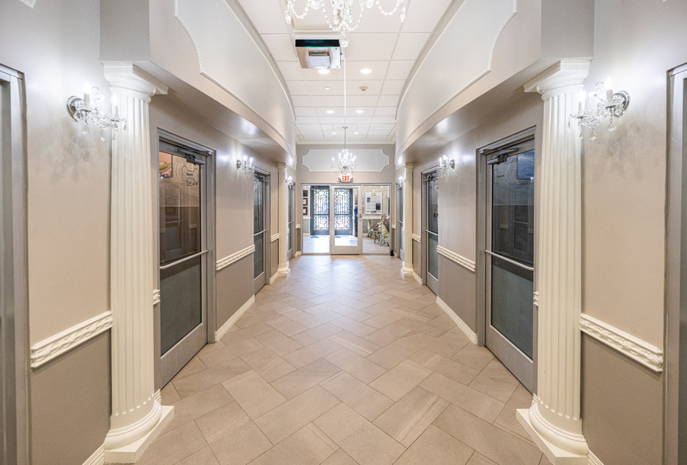 Elegant hallway with tiled floor, fluted columns, chandeliers, and frosted glass doors.