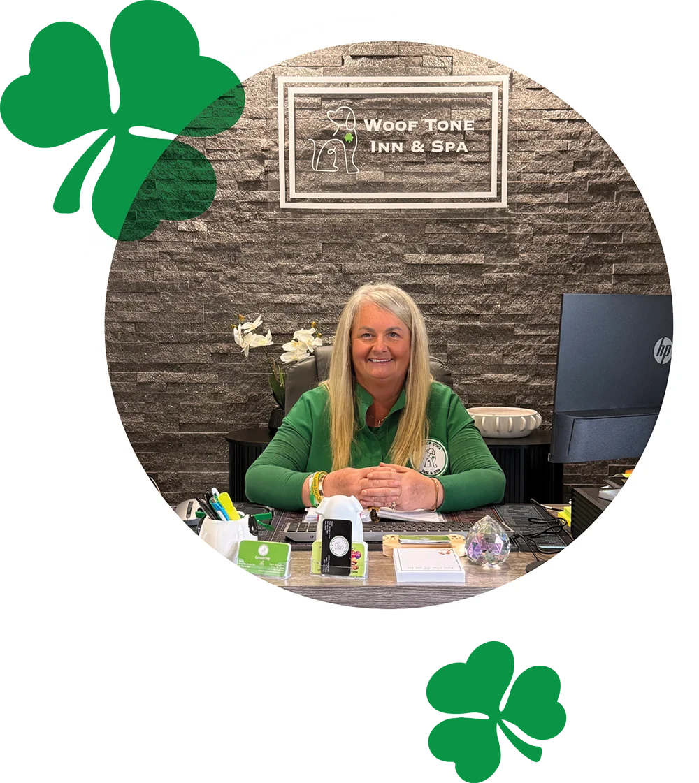 A woman in a green shirt sits at a desk in front of a stone wall with the "Woof Tone Inn & Spa" sign.